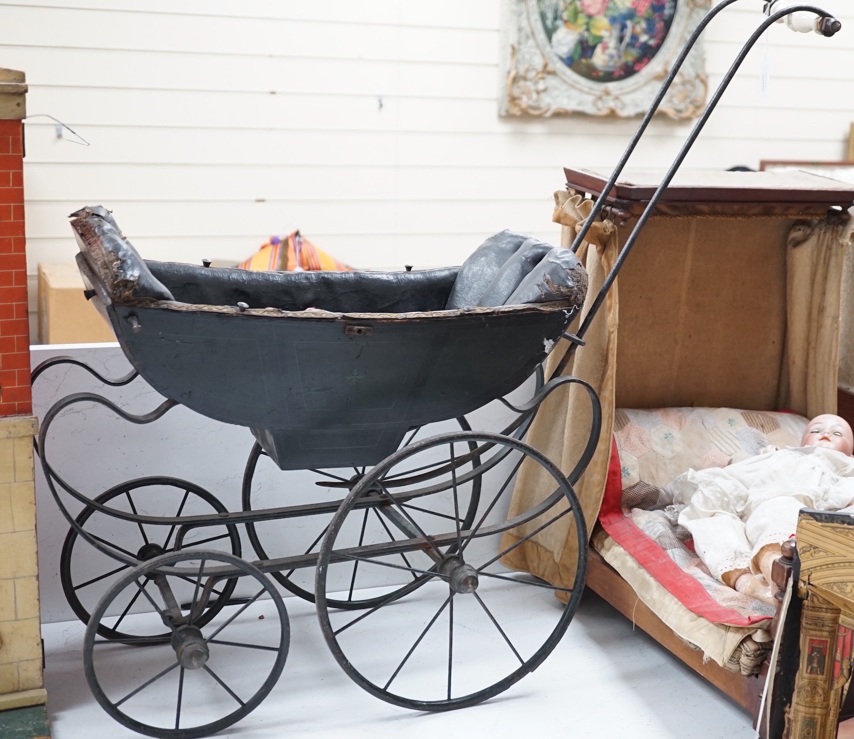 A late 19th century dolls’ pram, circa 1880, on a wrought iron chassis with spoked wheels, upholstered interior and porcelain handle, 75cm high, 90cm long